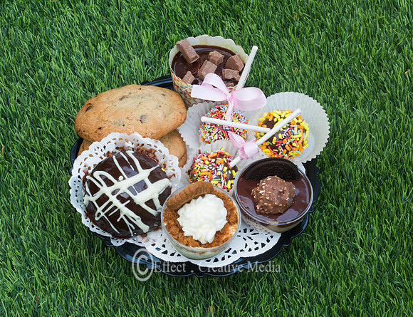 small chocolate cakes and cookies on a plat, sited on a grass